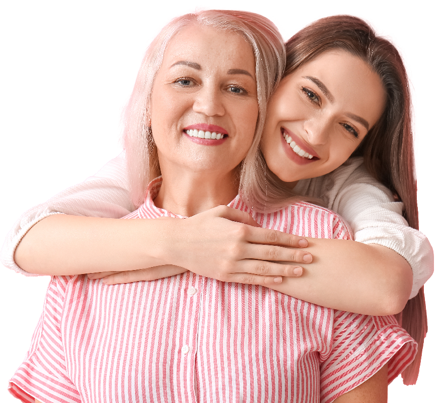 Two women smiling in front of a pink background. One is older, wearing a pink and white striped shirt, with short blonde hair. The younger woman, with long brown hair and a white top, hugs the older woman from behind.